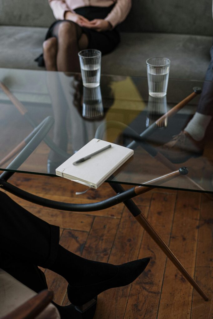 pexels-photo-4098232-4098232 Close-up of a counseling session with two glasses of water and a notepad on a glass table.